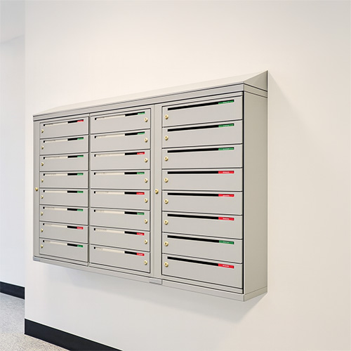 Väggmonterad fastighetsbox inomhus från Boxicon i ljusgrå kulör Väggmonterad fastighetsbox i silvergrå färg med flera postfack, installerad i ett trapphus för BRF eller hyresfastighet.